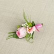Set gently atop an oatmeal-hued linen, this exquisitely detailed boutonniere is the embodiment of Tottenham's welcoming spirit and dedication to floral artistry. The arrangement features a tightly wound pink rose at its core, each petal softly graduating from vibrant blush at the heart to the faintest pink near the edges, imparting an air of newly opened beauty and quiet anticipation. Alongside, a peach-hued alstroemeria or similar flower gently spreads its petals, flecked with yellow and finely traced with natural markings, which add both warmth and detail to the ensemble. Baby's breath weaves through the composition with cloudlike delicacy, while petite green cushion mums nestle in for texture and lively contrast, recalling the lush pockets of nature around Tottenham Marshes. The greenery-ranging from slender, spiky grasses to broader dark green leaves, some artfully folded-frames the florals, creating a structure that is both lush and refined. A vibrant fuchsia pink satin ribbon wraps the stems at the base, tied neatly in a shining bow, elevating the entire piece with a festive and polished finish. Illuminated by gentle, even light, every subtle hue, whisper of green, and polished ribbon is revealed. This handcrafted floral accessory, ideal for weddings, proms, or important occasions in North London, evokes heartfelt celebration, a sense of new beginnings, and the timeless elegance synonymous with Tottenham's local floral traditions.