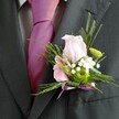 There's an understated magic in this Tottenham wedding buttonhole, where traditional tailoring meets contemporary floral artistry. Captured in intimate detail, the wearer's crisp charcoal suit and vivid magenta tie contrast beautifully, setting the stage for a florist's masterpiece pinned with care to the lapel. The centrepiece-a blush-toned rose-unfolds with grace, its petals radiant with the softness of early June sunlight reminiscent of mornings at Bruce Grove. Side by side with the rose blooms an alstroemeria, its striped magenta and pink petals hinting at playful sophistication, while a zingy green button mum surprises the eye with its lively, youthful energy. Dainty clusters of pure white gypsophila scatter a gentle, feathery elegance, reflecting the laughter and innocence that accompany Tottenham's festive gatherings. Framing the florals, an airy sweep of asparagus fern and delicate leafy strands supply layered texture and natural rhythm, much like the canopy found along Philip Lane's avenues. Securing the stems, a gleaming pale lavender ribbon is neatly tied, thoughtfully echoing the joyful pinks above and completing a vision of harmony. The composition is touched by soft ambient light, casting subtle shadows that lend depth and subtlety. Altogether, this buttonhole arrangement crystallises the spirit of a Tottenham wedding-filled with affection, individuality, and an artisan's assurance that every detail holds heartfelt meaning.